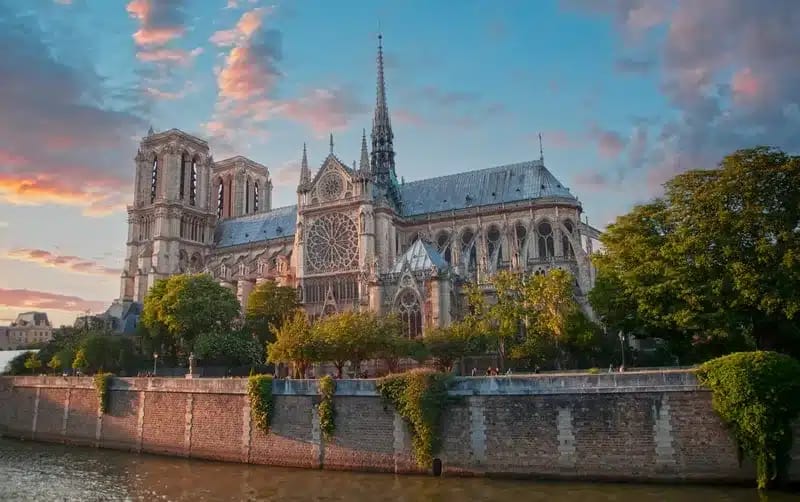 a large building with a spire and trees by a body of water Notre-Dame de Paris